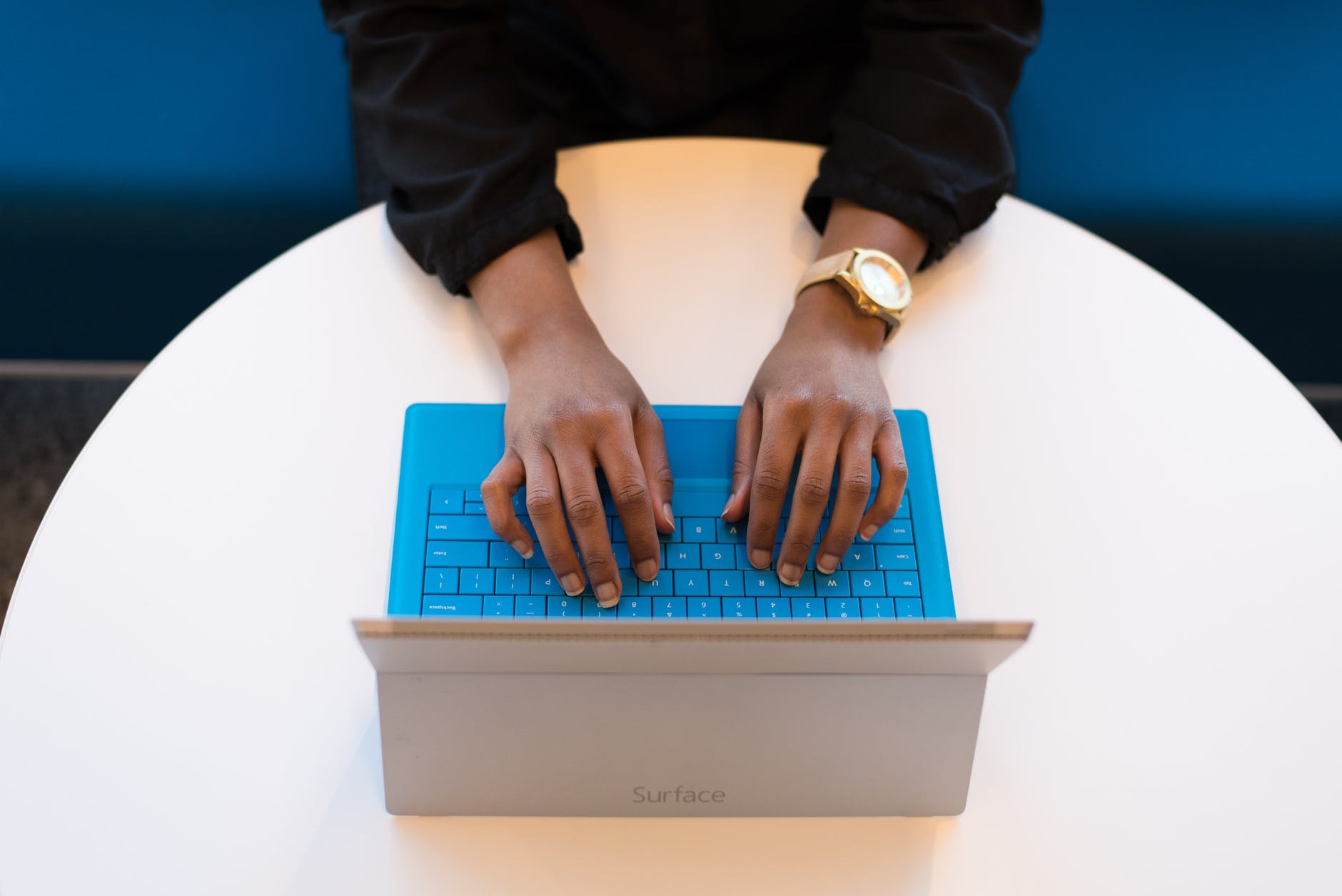 Photo of brown-skinned hands typing on a Microsoft Surface tablet with keyboard attached.