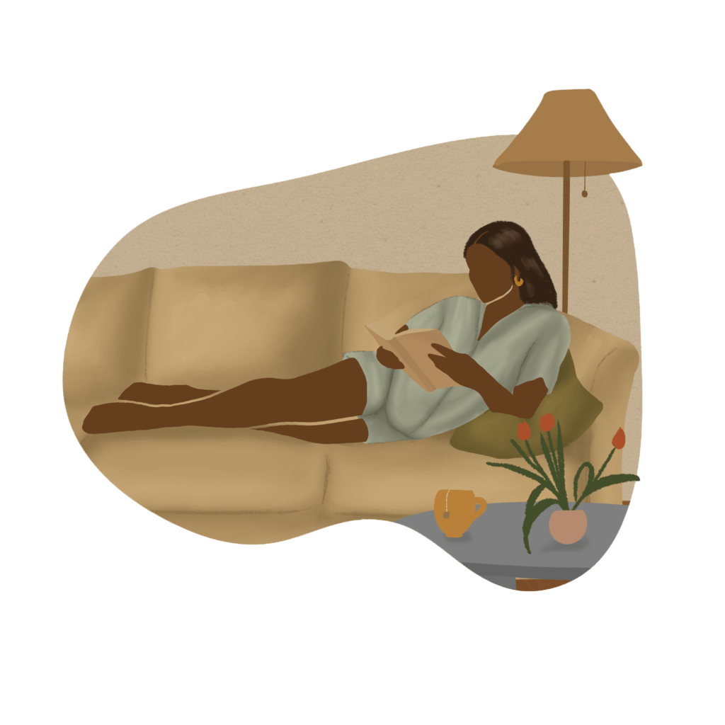 A woman of color in pajamas lying on a beige couch reading with a cup of tea sitting on a table in front of her.